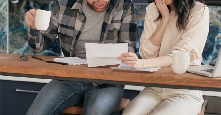 AC Budget - A Couple Sitting Near the Wooden Table while Looking at the Document in Shocked Emotion