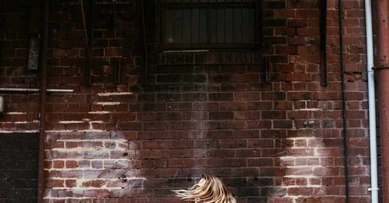 AC Cooling Systems - Side view of unrecognizable female with flying hair standing on street near aged house with air conditioning units in city